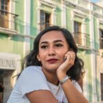 A young woman in a white t-shirt posing outdoors in a historic city setting.